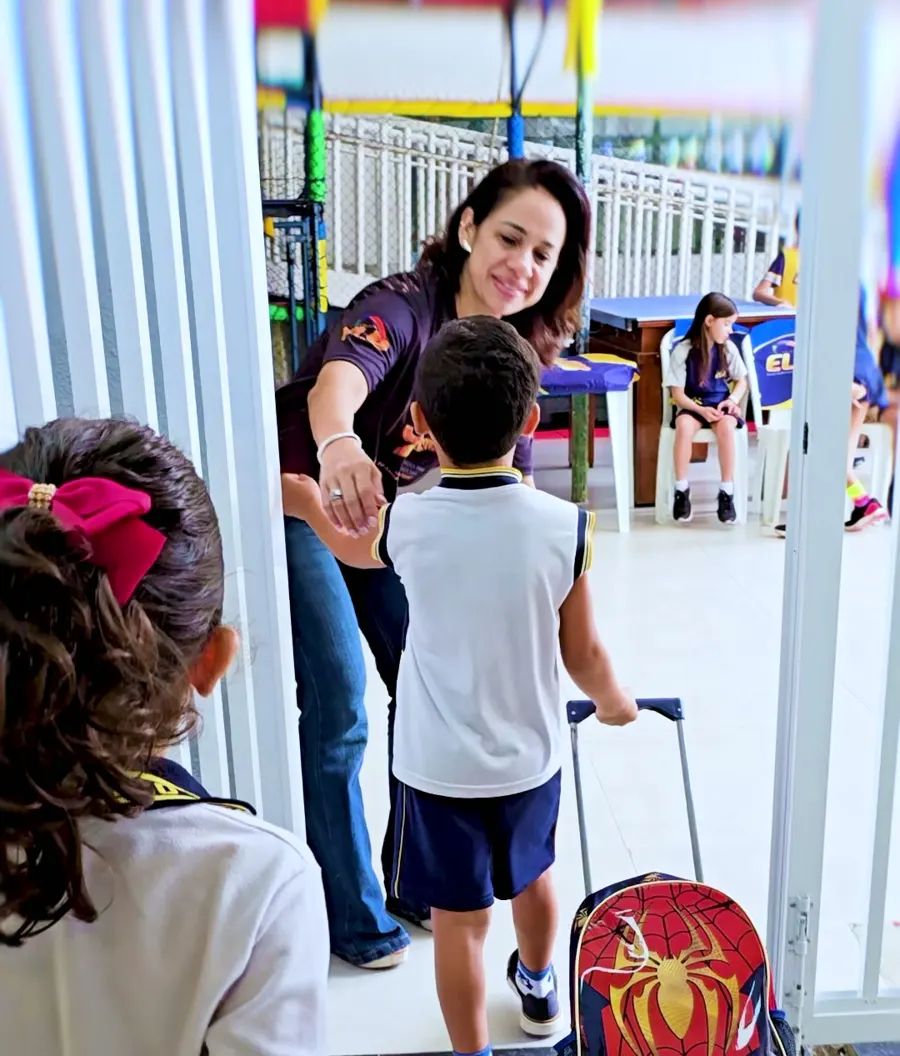 Professora recebendo um aluno na entrada da escola